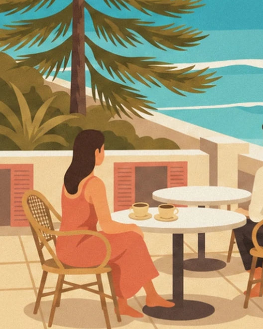 Een vrouw in een koraalrode jurk aan een tafel met 2 koppen koffie, met uitzicht op de zee