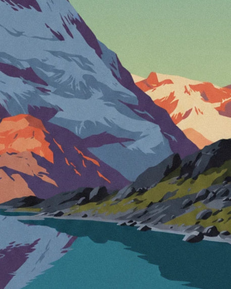 The rocky shore of the alpine lake, between green grass and snow-covered mountains