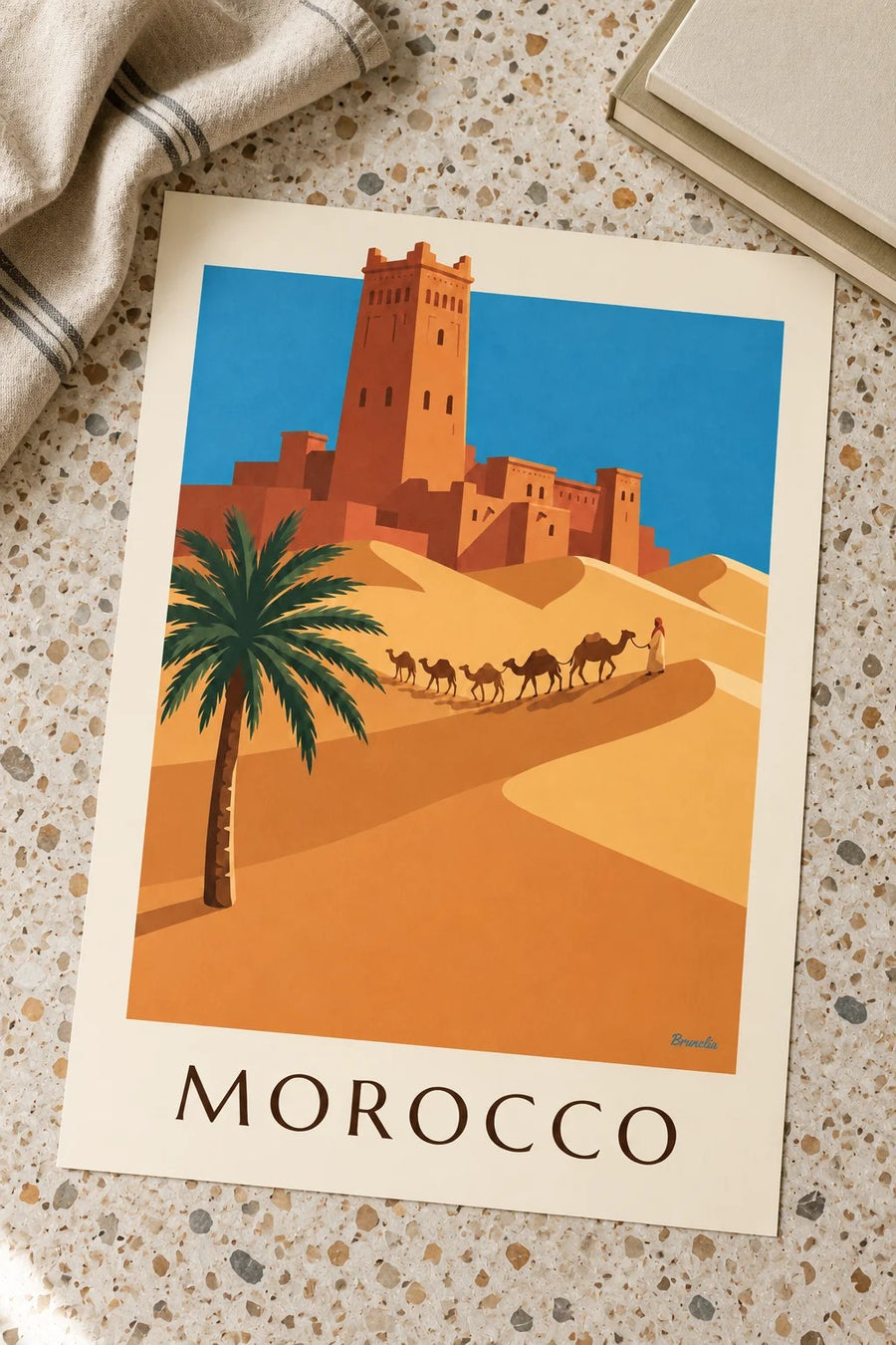 Affiche casbah et caravane de chameaux dans le désert marocain : posée sur une table